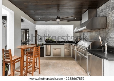 Modern outdoor kitchen and. luxury with grill, stove, extractor hood, wooden ceiling with fan, wooden tables and benches, chop tap, tiled wall.
Located in Coral Gables, Miami, FL, USA Royalty-Free Stock Photo #2288667853
