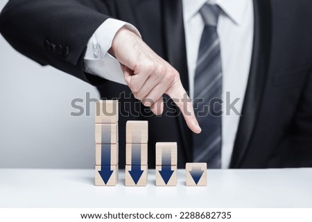 Wooden blocks with dark blue arrows icons, businessman in suit pointing down against white background, business decline loss drop concept