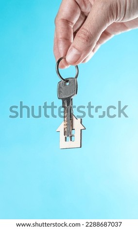 The hand holds a key with a keychain in the form of a house on a blue background Royalty-Free Stock Photo #2288687037