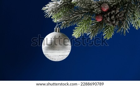 White silver ball on a snow-covered branch of a Christmas tree on a blue background, space for text