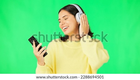 Happy woman, phone and dancing with headphones on green screen for audio track against a studio background. Female with headset listening to music on smartphone enjoying dance to sound on mockup