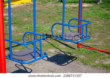 This photo features a pair of blue metal swings on a playground, with the clear blue sky in the background, evoking a sense of joy and freedom.