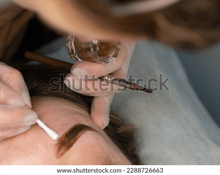 Close up of beautician's hand with brush tinting eyebrows in beauty salon . High quality photo