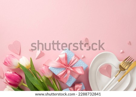 Festive Mother's day table arrangement. Top view flat lay of plates, cutlery, tulips, gift boxes, and decorative hearts on pastel pink background with a space for promotional content or text