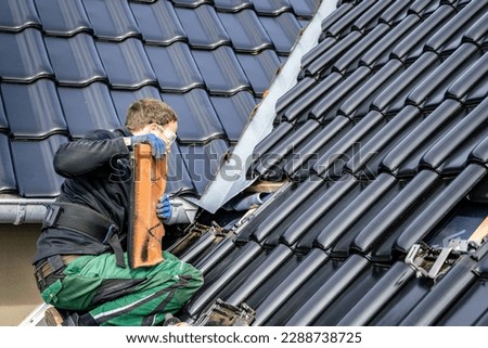 Craftsman removing tiles from a roof to install brackets for solar panels Royalty-Free Stock Photo #2288738725