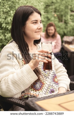 Portrait of beautiful brunette woman and new mother looking away holding a non-alcoholic drink in a beer garden at the pub after a walk with her family. Spring season in Scotland. Leisure and relax.