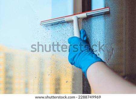 Window washing. Window cleaning with a squeegee and a wiper on a sunny day close-up. Dirty windows. Royalty-Free Stock Photo #2288749969