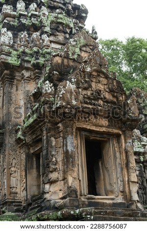 A photo of the doorway leading into the main sanctuary at the Thommanon Temple in Angkor Archaeological Park, Cambodia. The base of the tower is visible along with decorative bas reliefs of devatas. 