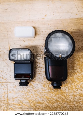 A classic, small photo reporter lamp with a diffuser next to a contemporary, large lamp with a round head