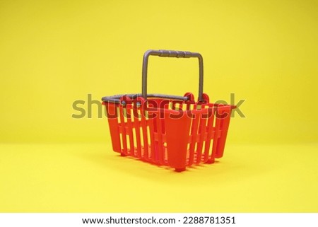 Empty red shopping basket on yellow background.