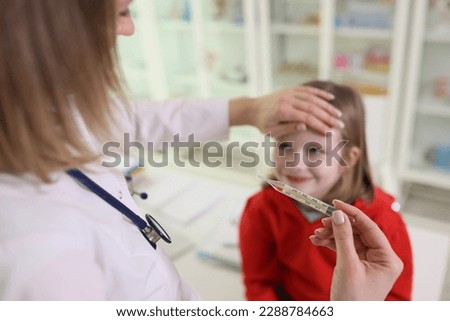 Doctor puts hand on forehead of junior schoolgirl looking at mercury thermometer. Woman in uniform measures temperature of child in clinic