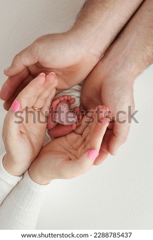 Feet, toes, heels of a newborn. Children's foot in the hands of mother, father, parents with a knitted pink heart. The legs of the child in the arms of mom and dad. On a white background. Royalty-Free Stock Photo #2288785437