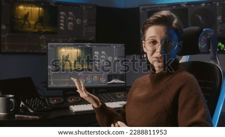 Young female video editor records for blog, talks about films color correction. Software interface with color wheels and movie footage on computer monitor and big screens. Color grading control panel. Royalty-Free Stock Photo #2288811953