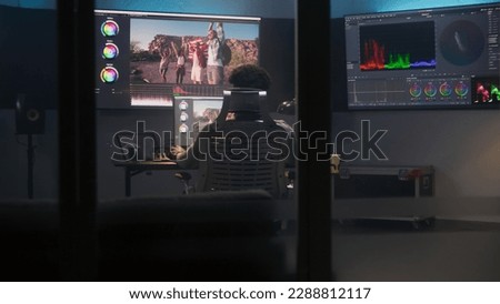 African American colorist does color grading in professional software on computer. Process of colour correction for video post production in modern studio. Multiple monitors with travel movie footage.