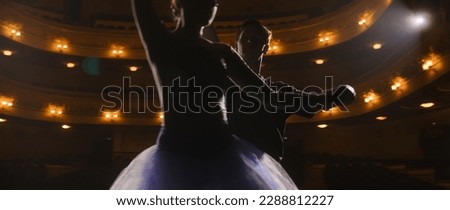 Beautiful ballet dancers talk and practice ballet movements during choreography rehearsal on theater stage illuminated by spotlights. Man and woman prepare dance performance. Classical ballet dance.