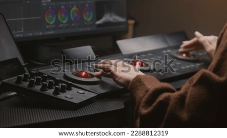 Female editor uses digital color correction control surfaces in studio. Colorist makes video or photo color grading on computer. Software interface with RGB graphics and color wheels on PC monitor.