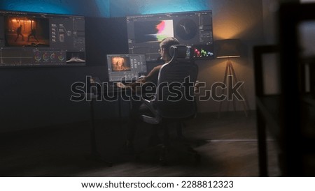 Female film editor or colorist does color grading on computer in modern studio. Big monitors with RGB colour correction graphic bar and program interface on the wall. Video post production. Handheld.