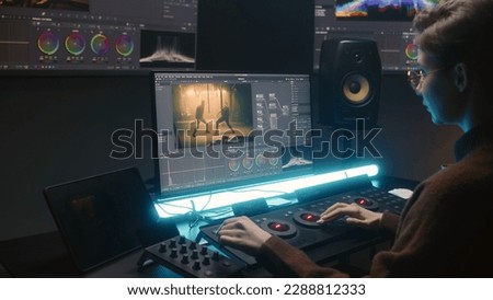 Female editor uses color grading control panel, edits video, makes movie color correction on computer and tablet in studio. Film footage and RGB wheels on monitor. Big screens with program interface.