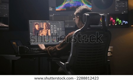 Female editor works in modern studio on computer using professional editing software. Woman edits video footage, makes color grading for movie post production. Big screen with RGB graphic on the wall. Royalty-Free Stock Photo #2288812423