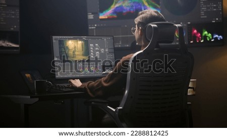 Female editor works in modern studio on computer using professional editing software. Woman edits video footage, makes color grading for movie post production. Big screen with RGB graphic on the wall. Royalty-Free Stock Photo #2288812425