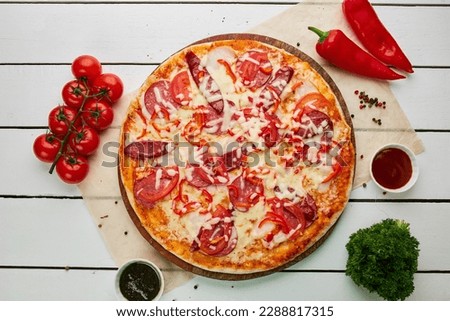 Freshly baked pizza with smoked sausages, red pepper and tomatoes served on wooden background with sauce and herbs. Food delivery concept. Restaurant menu