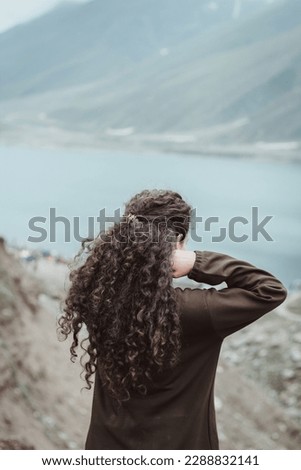 young curly hair woman in brown sweater hands adjusting hair enjoying scenery of fresh air clouds over the mountains in lake 