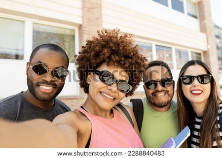 A diverse group of college students. The 4 young people take a picture with their smart mobile phone with sunglasses on. Concept of interracial university friends, multiethnic group