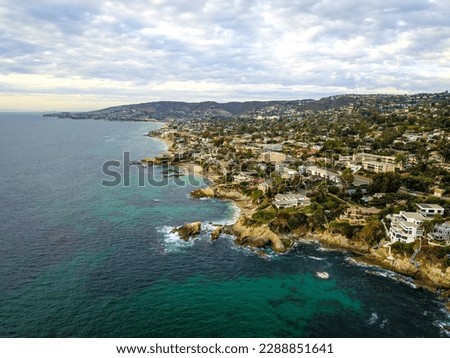 aerial shot of a gorgeous summer landscape along the coastline with blue ocean water and homes along the mountains surrounded lush green trees and plants at Victoria Beach in Laguna Beach California