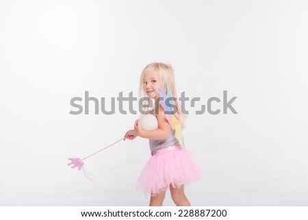 Half-length portrait of little fair-haired lovely smiling girl wearing pretty grey vest pink skirt and white wings going somewhere holding a magic wand looking at us