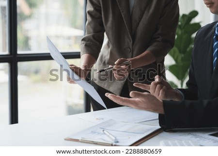 Asian business team pointing at the graph Data charts on chart documents discussing financial management, income, corporate taxes at office desk.