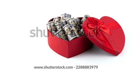 A gift box in the shape of a human heart filled with banknotes of 100 American dollars on a white background.