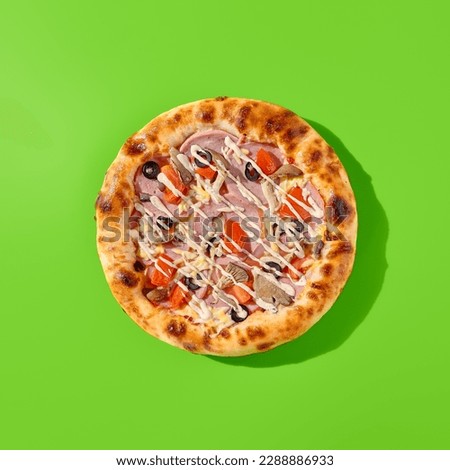 Thick-crust pizza with ham, mushrooms, and olives on a bright green background. Minimalist style, top view of pizza, junk food. Royalty-Free Stock Photo #2288886933
