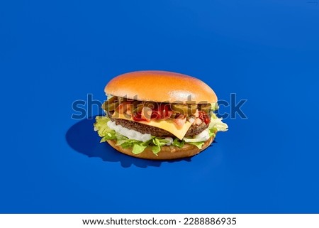 Tasty beef burger on blue backdrop, featuring jalapeno peppers, vibrant greens, minimalist design, contemporary food photo, perfect for grab-and-go, horizontal layout, tempting meaty treat.