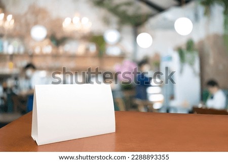 Blank menu frame label mockup. Mock up menu frame on table in bar restaurant, stand for booklet with white sheet of acrylic tent card paper in blur cafeteria, cook chef in background.