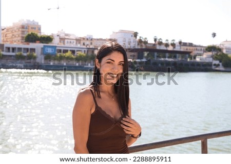 young and beautiful woman from south america and dressed in short dress is on vacation in seville. In the background the river. The woman smiles and makes different expressions. Travel and vacation.