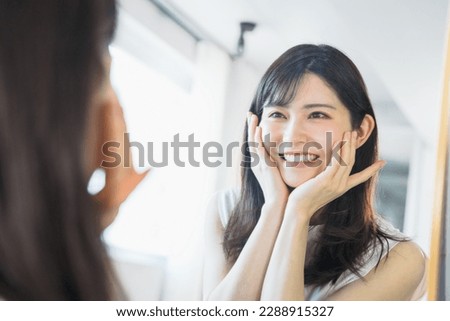 Looking at my face in the mirror, I am happy with the good skin condition and put my hand on my cheeks with both hands (beauty image)