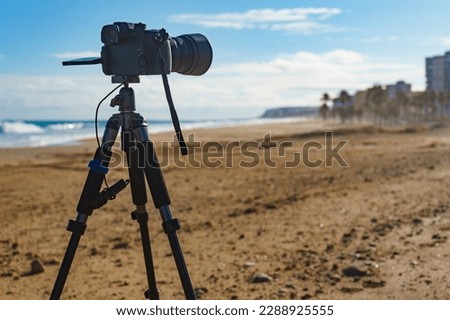 Professional camera on tripod taking picture film video of sea coastal landscape, Spain.