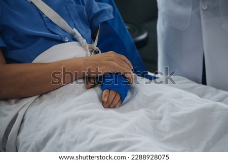 Injured patient showing doctor broken wrist and arm with bandage in hospital office or emergency room. Sprain, stress fracture or repetitive strain injury in hand. Nurse helping customer. First aid.