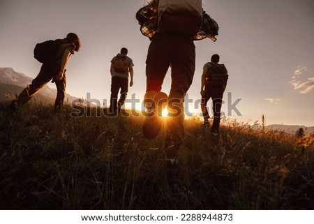 Silhouettes of four young hikers with backpacks are walking in mountains at sunset time Royalty-Free Stock Photo #2288944873