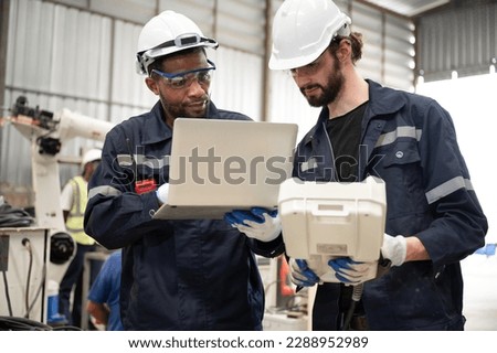 Caucasian and African American technician engineer man use remote control and computer notebook with checking machine arm robot at factory	