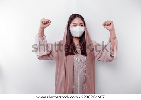 An Asian Muslim woman wearing a mask as a preventive for covid-19 is expressing a happy successful expression wearing a hijab isolated by white background Royalty-Free Stock Photo #2288966607
