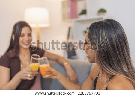 Elegant friends toasting with orange cocktail sitting on the sofa at home