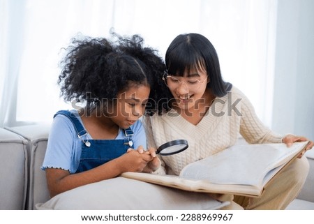 Asian kind mother teach her daughter using Focus glass on a book to see a tiny thing, relationship between mom and kid concept, mother's day concept.