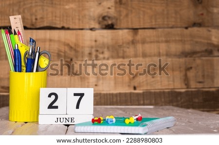 June calendar background with number  27. Stationery pens and pencils in a case on a wooden vintage background. Copy space notepad with pencils and calendar. Planner place for text.