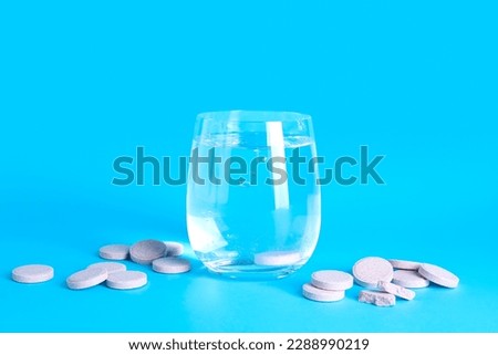 Glass of water with soluble tablets on color background