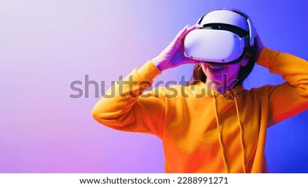 Young Caucasian beautiful woman wearing a yellow hoodie and VR headset, experiencing virtual reality with a red and blue neon light in the background, futuristic technology and wearable device concept