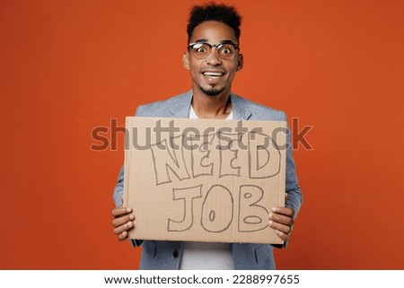 Young optimistic employee business man corporate lawyer in classic formal grey suit shirt glasses work in office hold cardboard sign card need job look camera isolated on plain red orange background