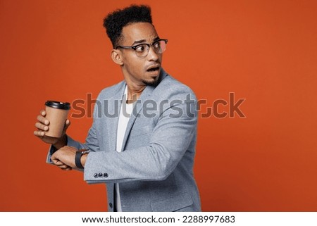 Young employee business man corporate lawyer wear classic formal grey suit shirt glasses work in office use smart watch check time hold cup of coffee run isolated on plain red orange background studio Royalty-Free Stock Photo #2288997683
