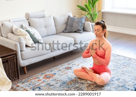 Woman is meditating at home. Woman in lotus position on the floor with her eyes closed and practices yoga meditation. Healthy lifestyle concept and home workout during quarantine.