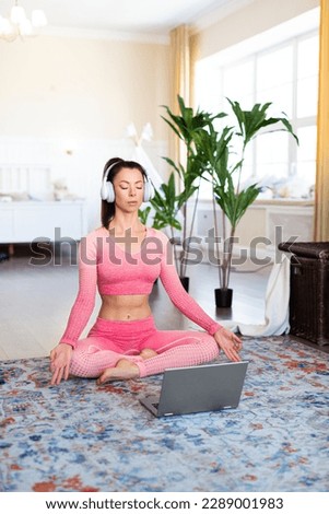 Vertical photo of a woman meditates at home in front of a laptop monitor. Online yoga lesson during quarantine. Healthy lifestyle concept.